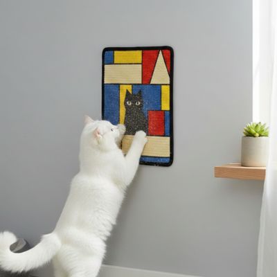 Chat blanc faisant ses griffes sur un griffoir mural décoratif coloré fixé sur un mur gris clair